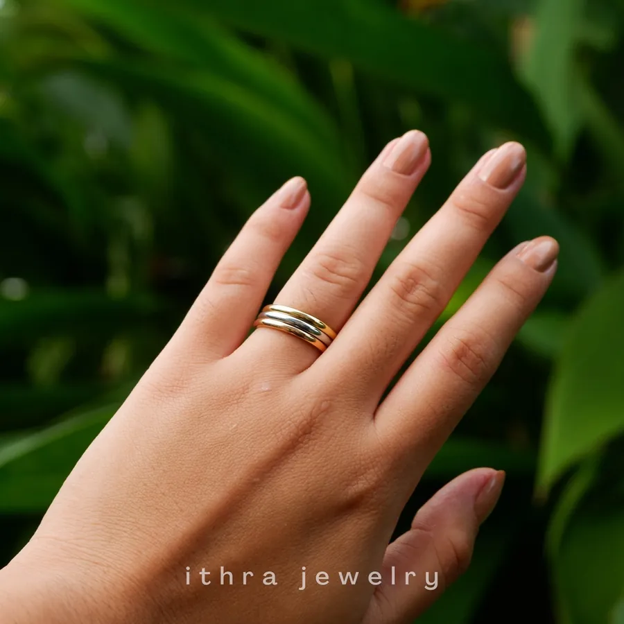 A hand wearing stacked gold rings against palm leaves