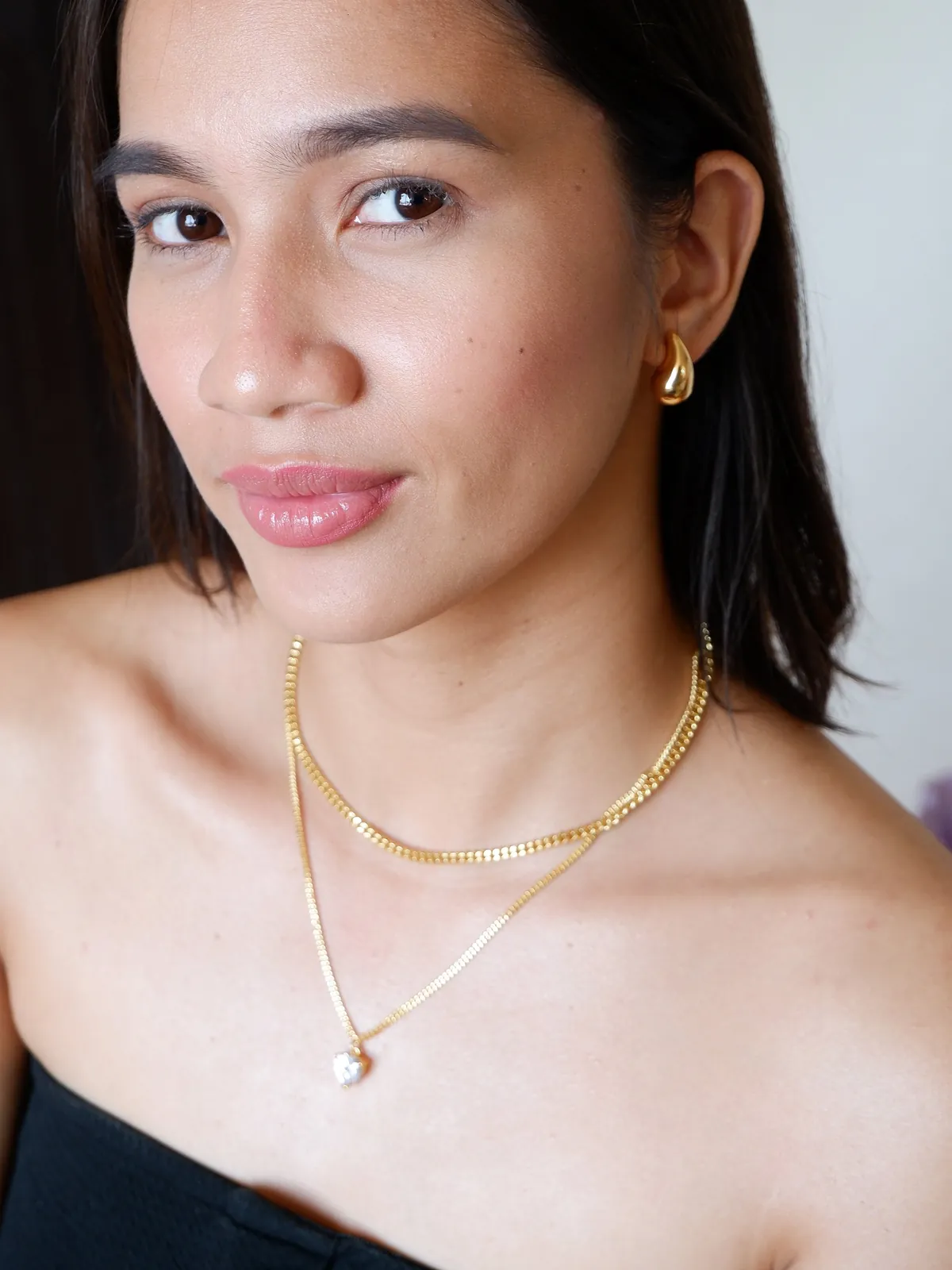 A woman wearing a gold pendant and small hoops