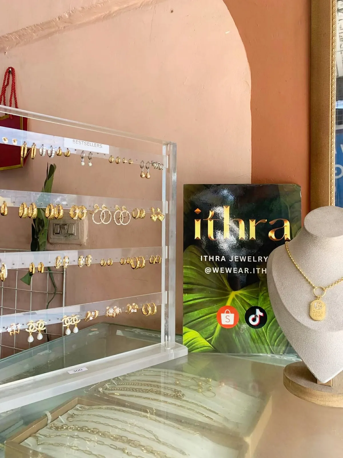 The ITHRA counter: acrylic earring racks, a necklace bust and the ithra sign against pink arches