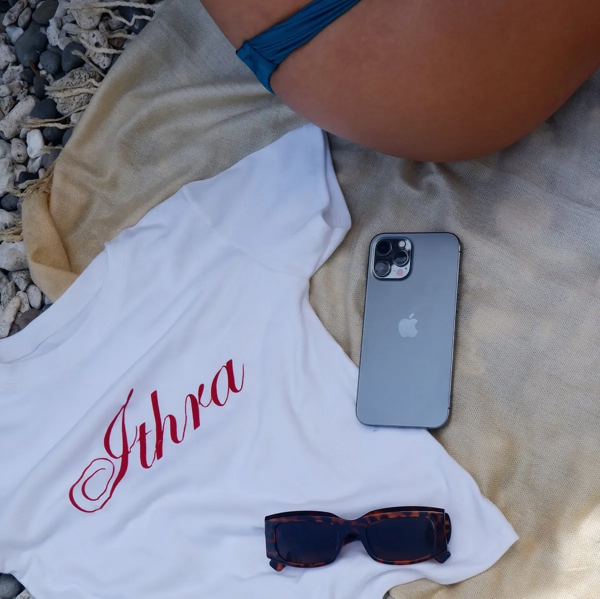 An ITHRA tee laid flat beside sunglasses